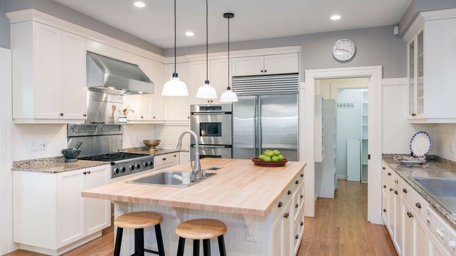 A kitchen with white cabinets , wooden counter tops , stainless steel appliances , and a large island.