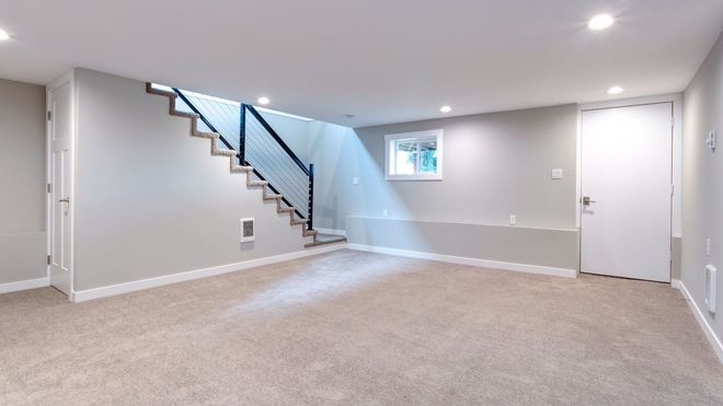 An empty basement with a staircase and a window.