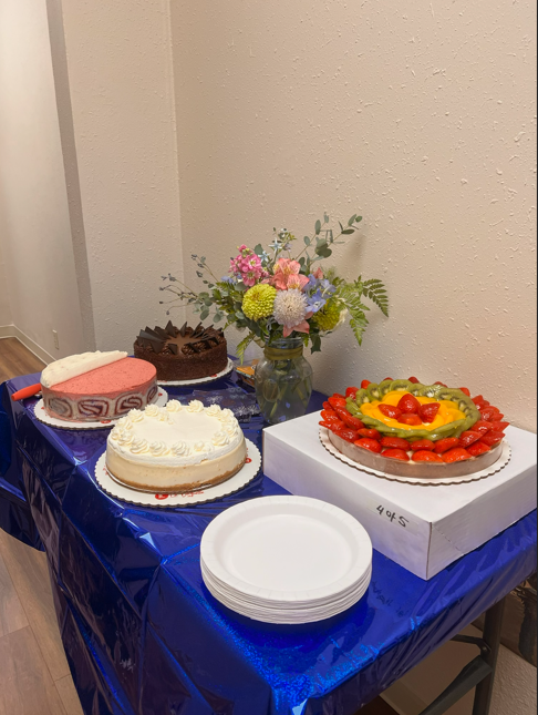 Desserts and fruit tarts on a blue-covered table with a flower vase in a corner room
