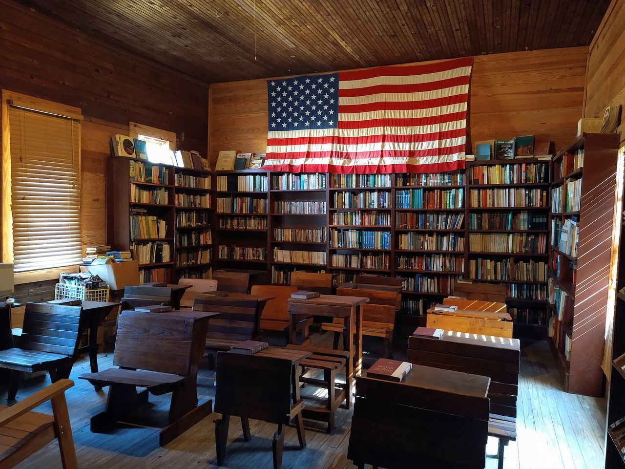 Interior of a library with rows of bookshelves, wooden desks, and an American flag.