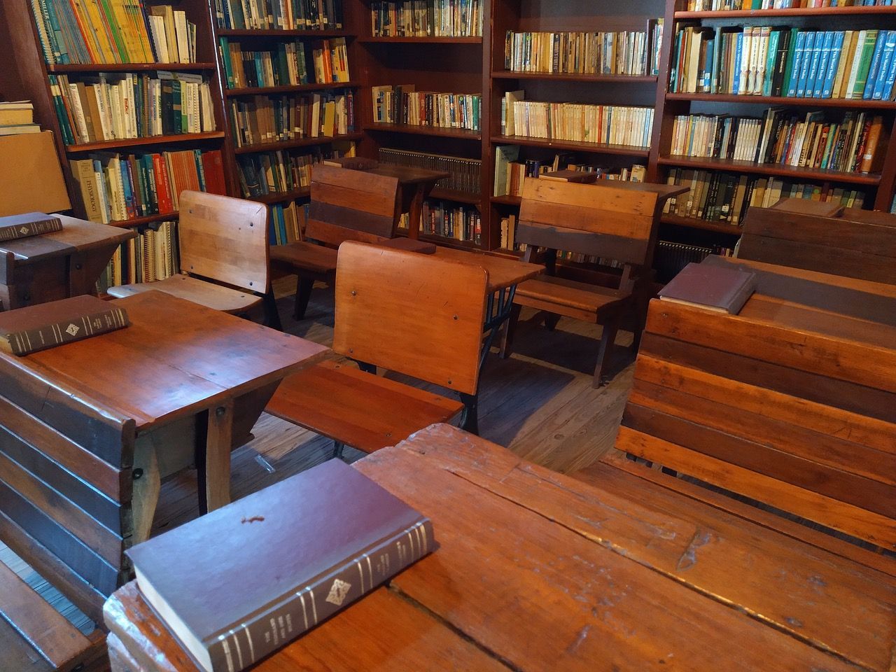 Wooden desks and chairs in a library, surrounded by bookshelves filled with books.