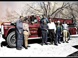 Firefighters pose by a red fire truck at Alapaha Fire Dept. in a vintage outdoor setting.