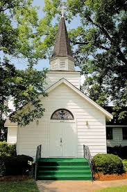 White church with a steeple, cross, and green steps, surrounded by trees.