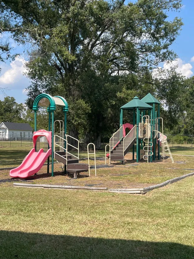 Playground with pink slide, green structure, and wooden stairs on a grassy field.
