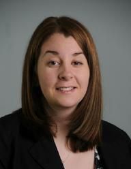 Portrait of a smiling person with shoulder-length brown hair against a gray background