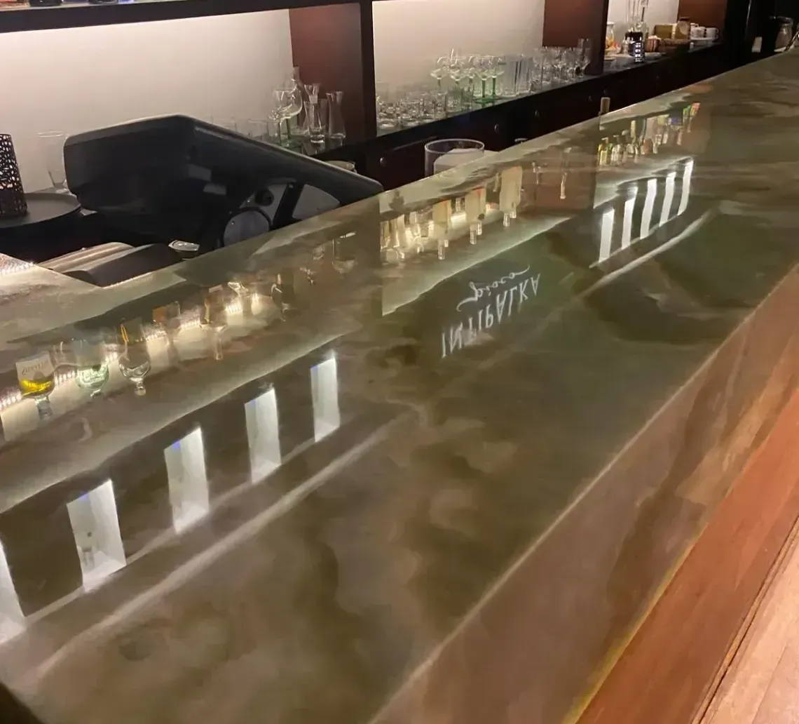 Bar with a green-toned, glossy counter reflecting the bottles and lights behind it. Wooden details.