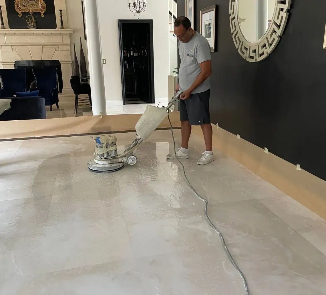 A man using a floor sander in a home. The floor is light, and the walls are dark.