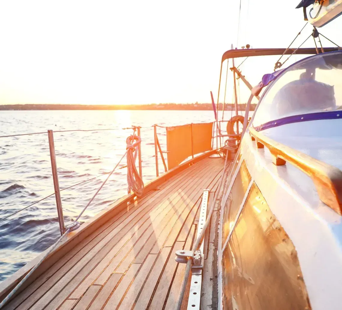 Wooden deck of a sailboat sailing on a body of water at sunset.
