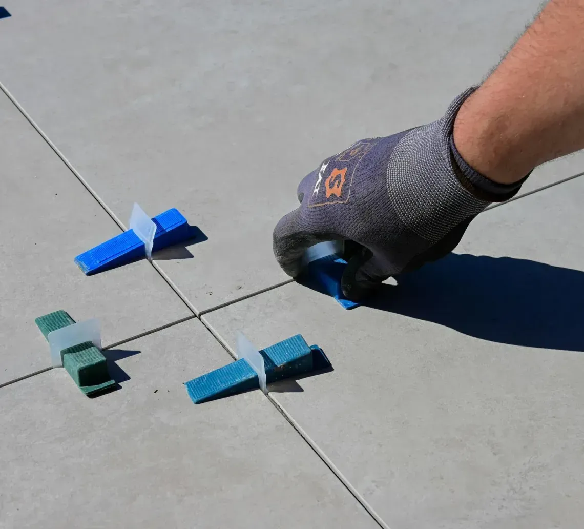 A gloved hand uses a blue tile leveling system on a concrete surface with tiled flooring.