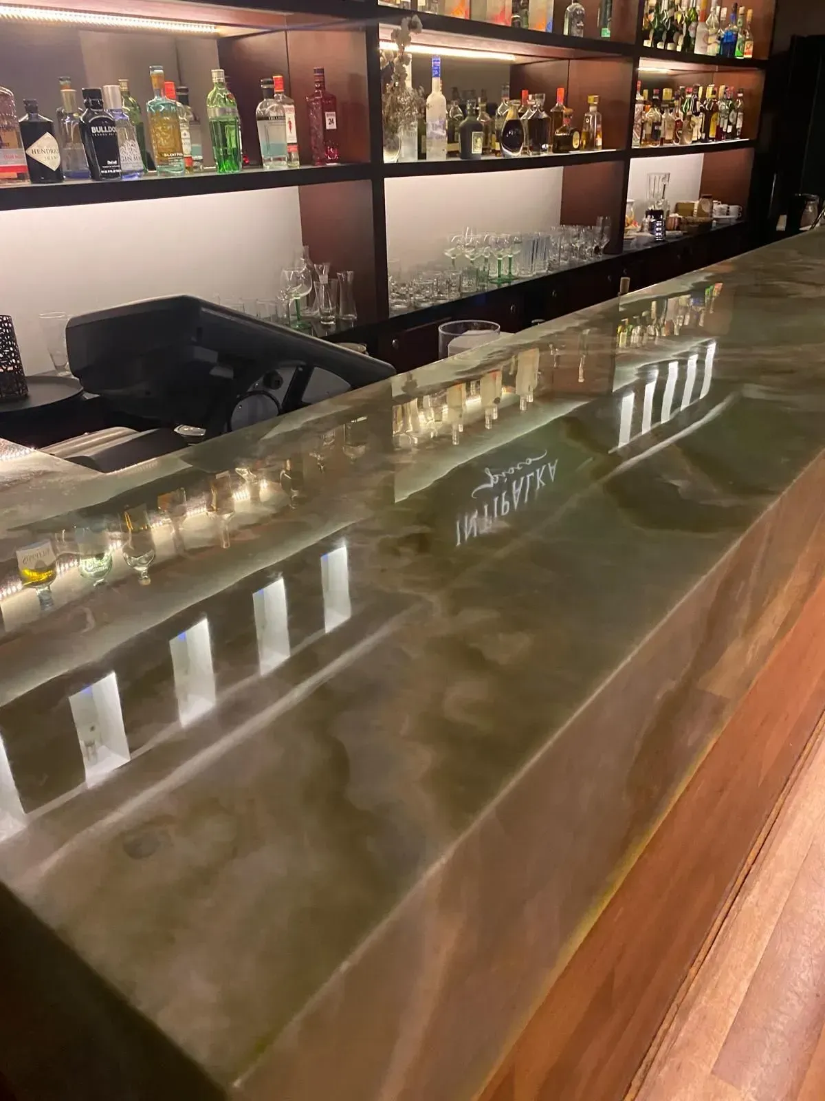 Bar with a green-toned, glossy counter reflecting the bottles and lights behind it. Wooden details.