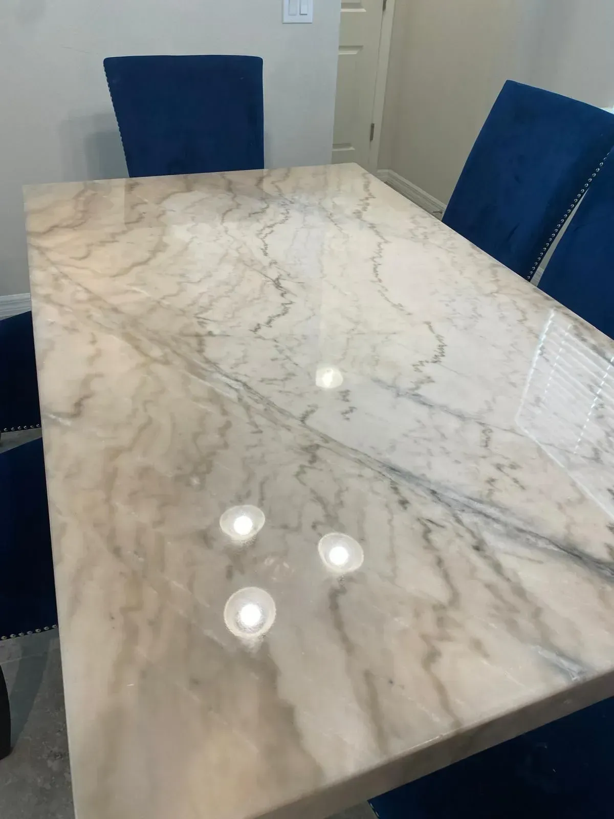 Rectangular marble dining table with four blue velvet chairs.