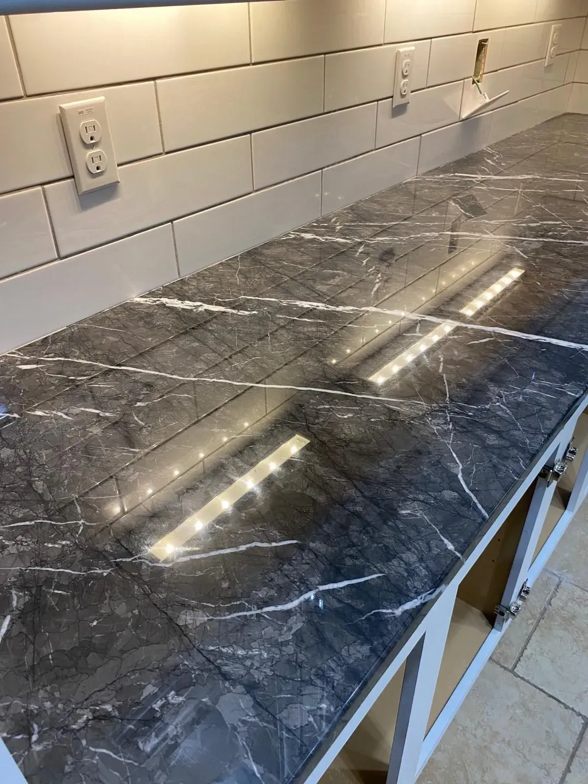 Dark gray marble-patterned countertop with white veining, under-cabinet lighting, white subway tile backsplash.