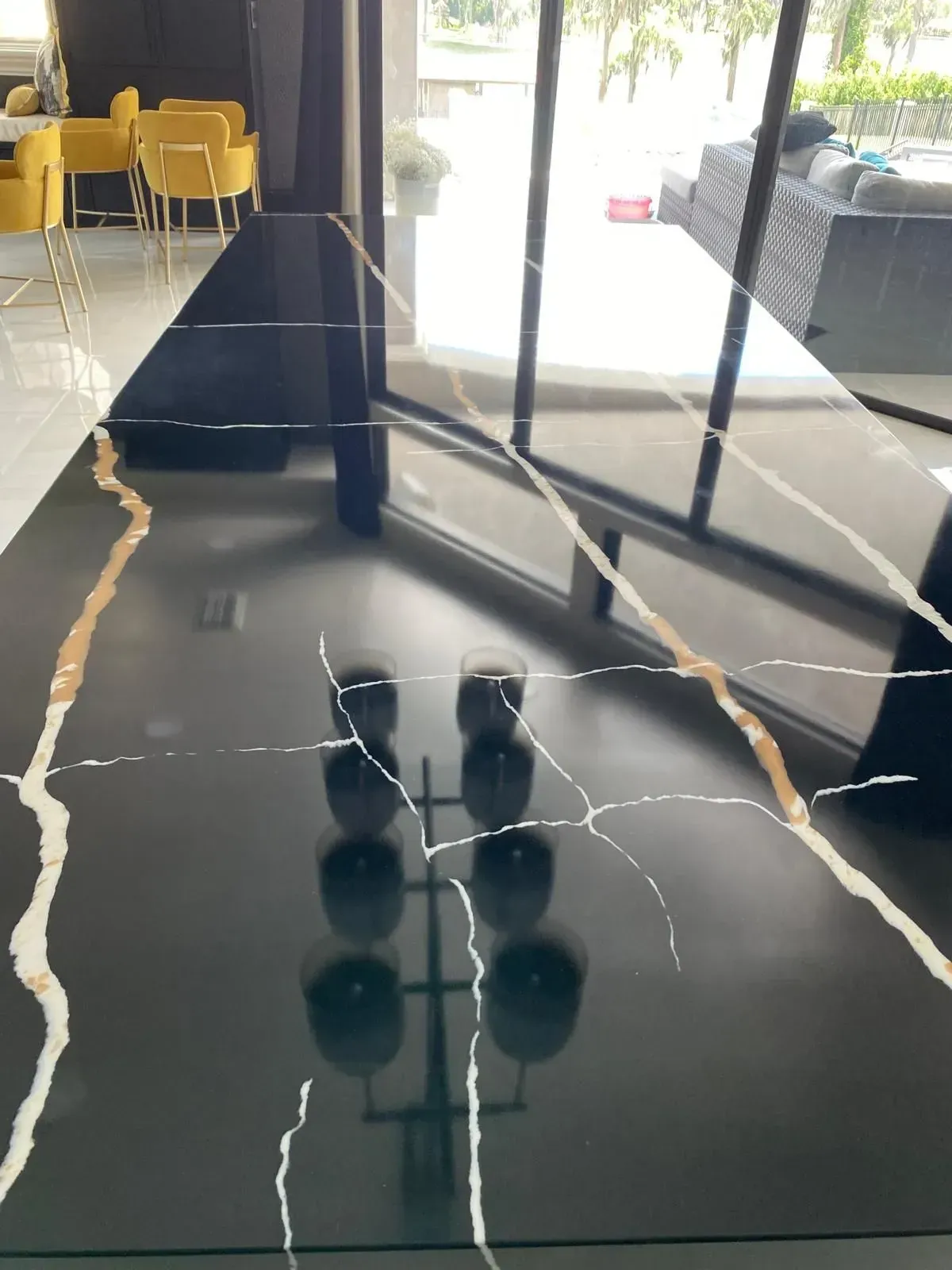 Black countertop with gold veining, reflection of interior with chairs and windows.