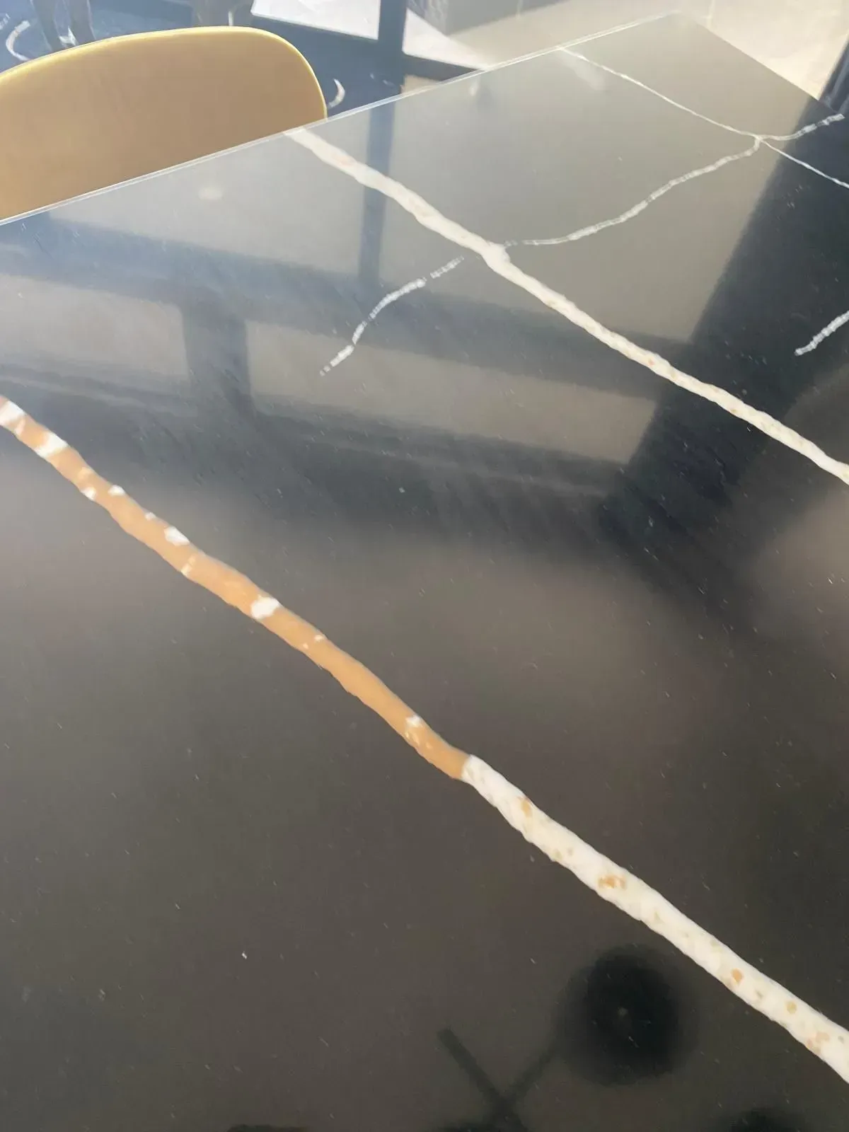 Close-up of a black marble table with white and tan veining. A yellow chair back is visible.
