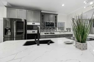 Modern kitchen with a white countertop island, stainless steel appliances, and gray cabinets.