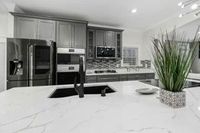 Modern kitchen with a white countertop island, stainless steel appliances, and gray cabinets.