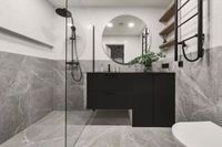 Modern bathroom with gray marble tile, black vanity, round mirror, and shower.
