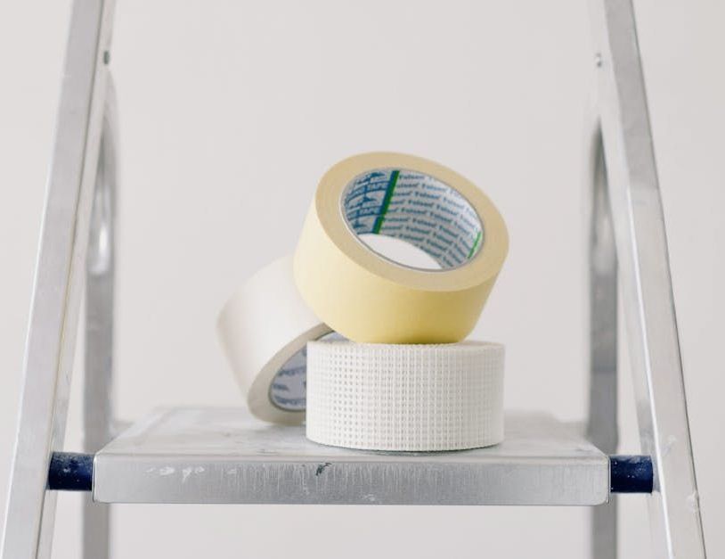 Three rolls of adhesive tape stacked on a white step ladder shelf