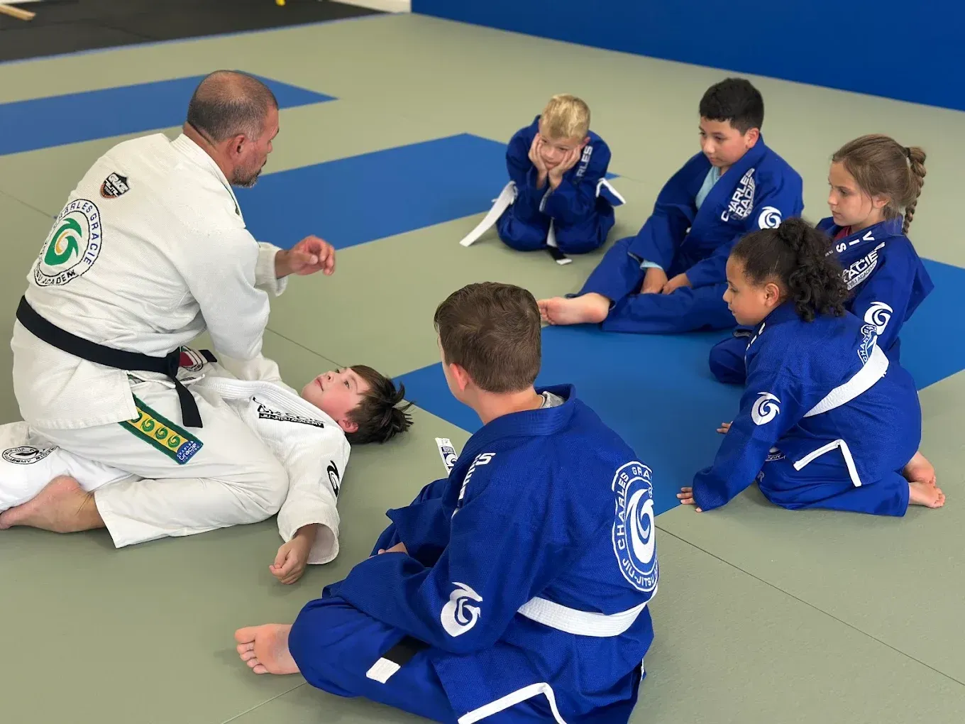 Instructor demonstrating technique to students in blue gis on mats at Charles Gracie Jiu Jitsu Magnolia, TX
