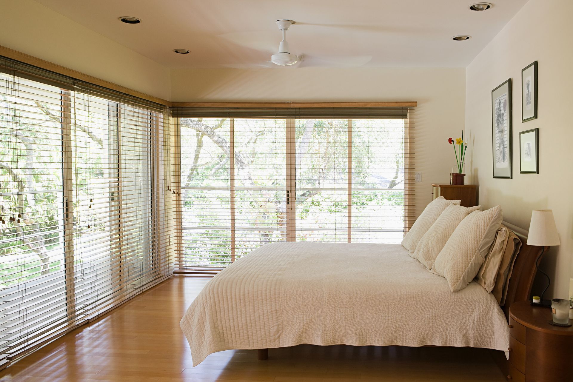 Bright bedroom with large windows, wooden floor, and a white bed by framed wall art