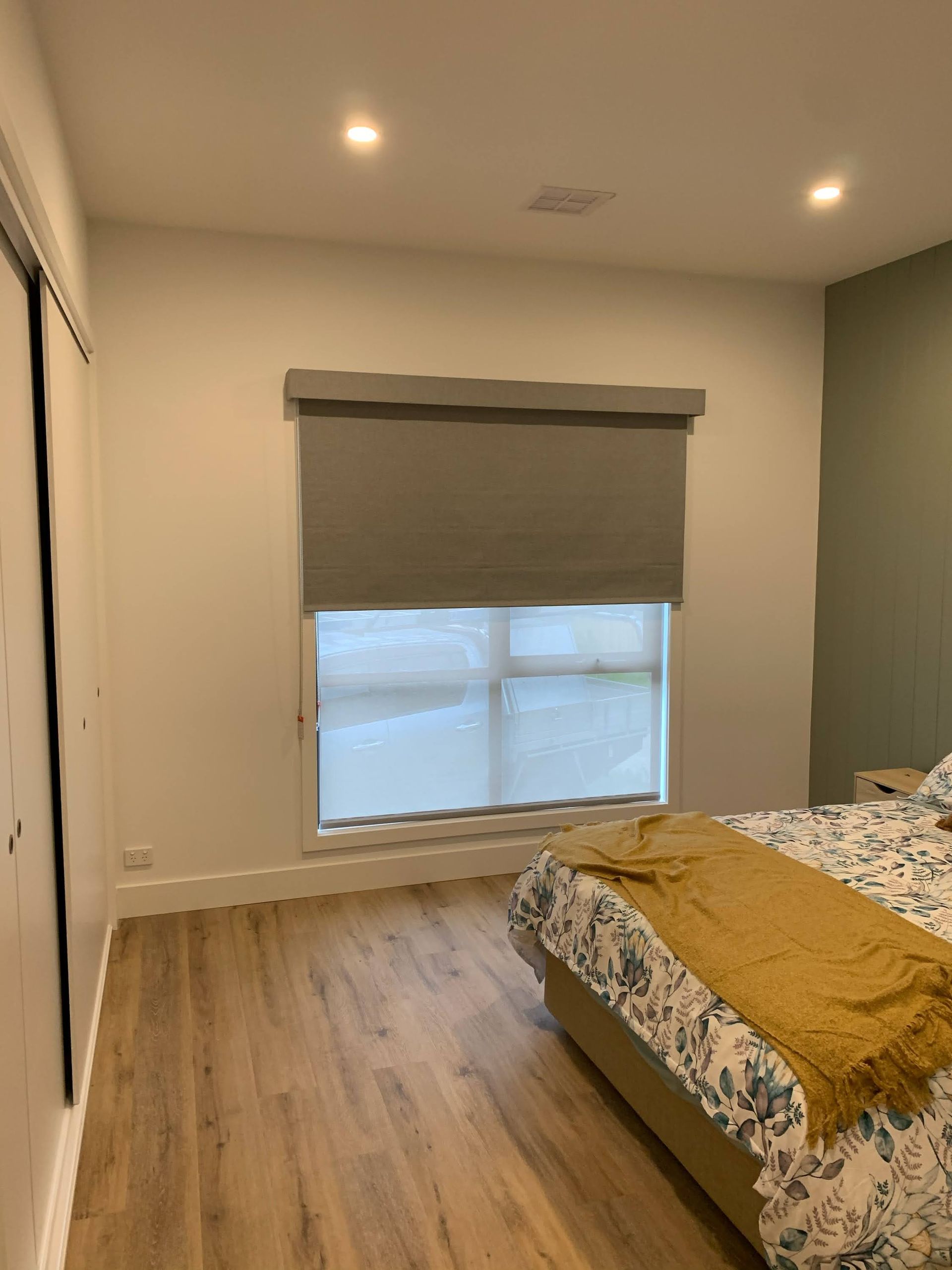 Bedroom with a bed, wood flooring, and a window with a gray blind.