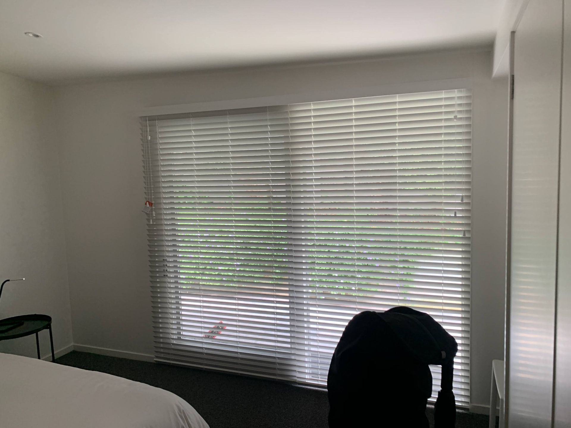 Empty room with large window blinds and a black chair in the foreground.