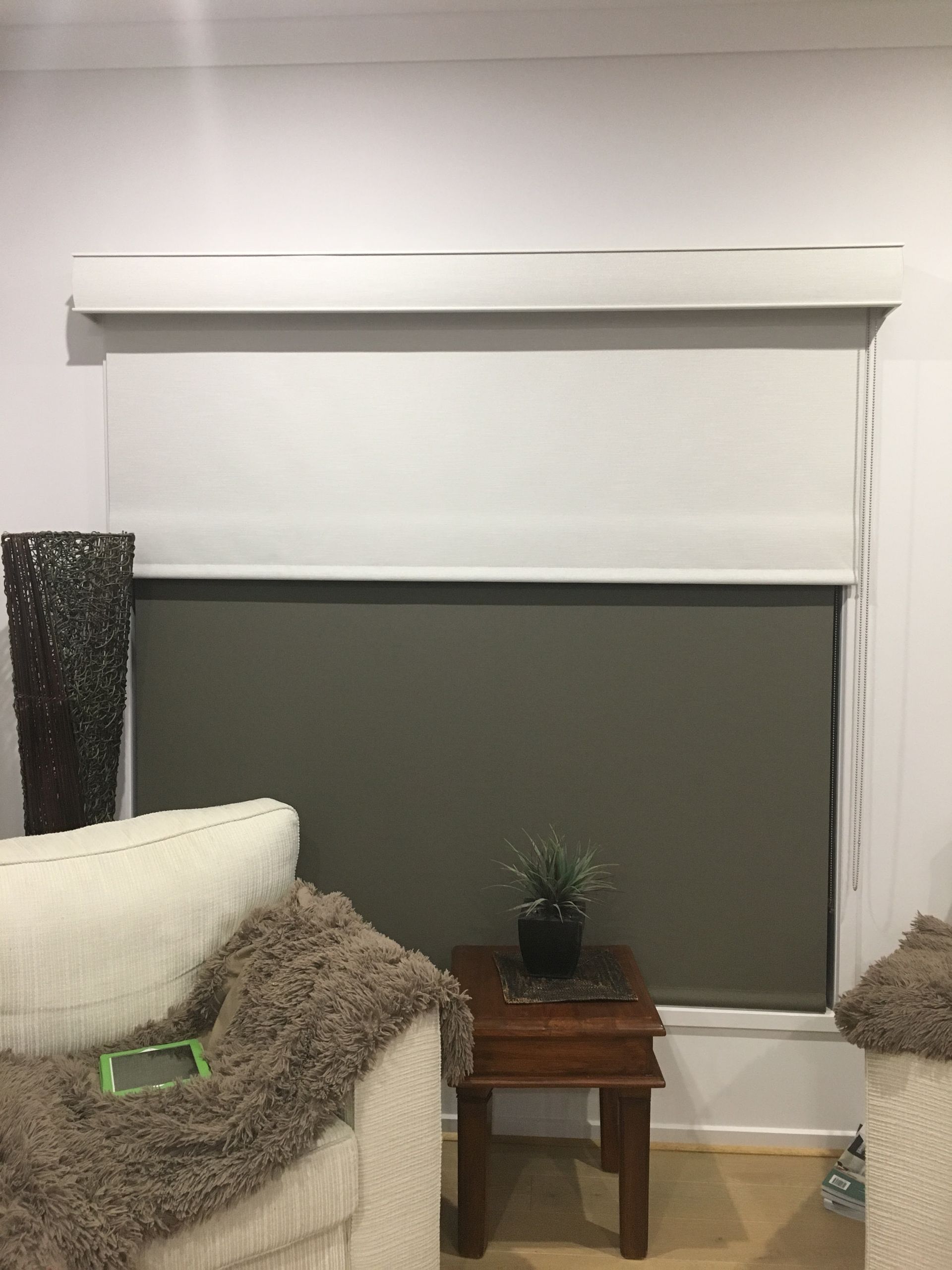 Living room window with white blind, gray shade, sofa, and small wooden table with a plant