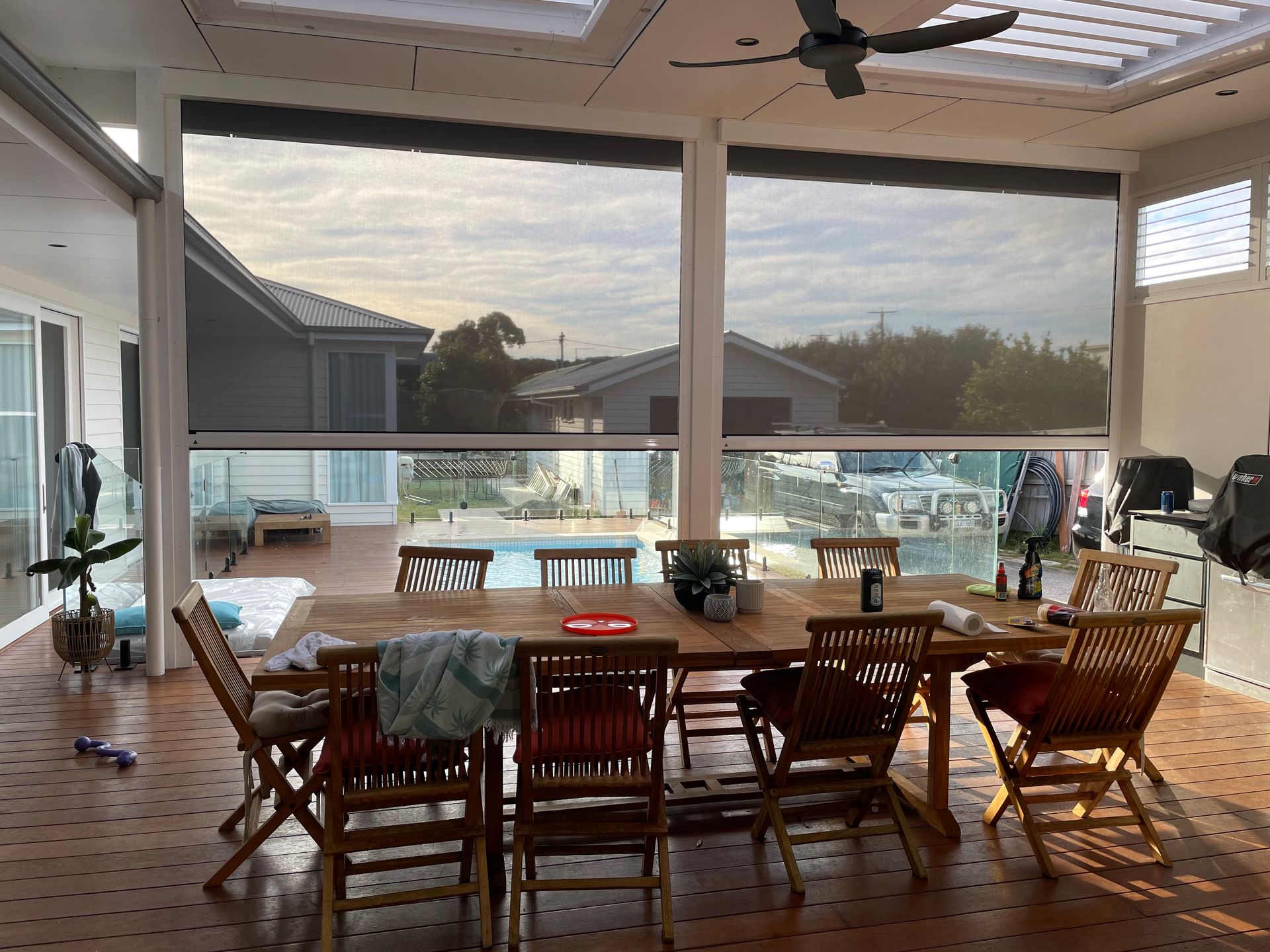 Screened patio dining area with table, chairs, ceiling fan, and view of outdoor pool at sunset