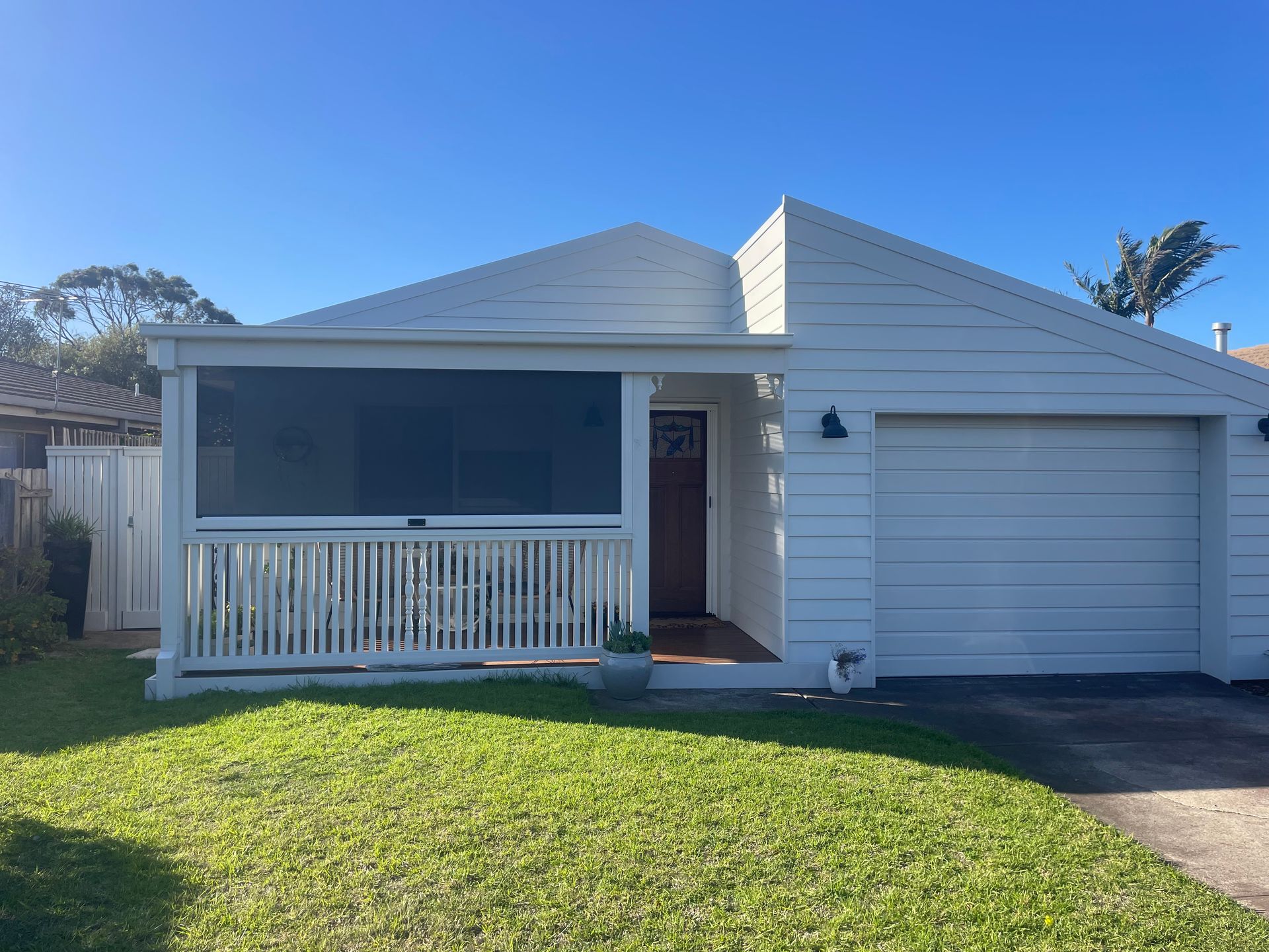 Small white house with a garage, front porch, and green lawn under a blue sky