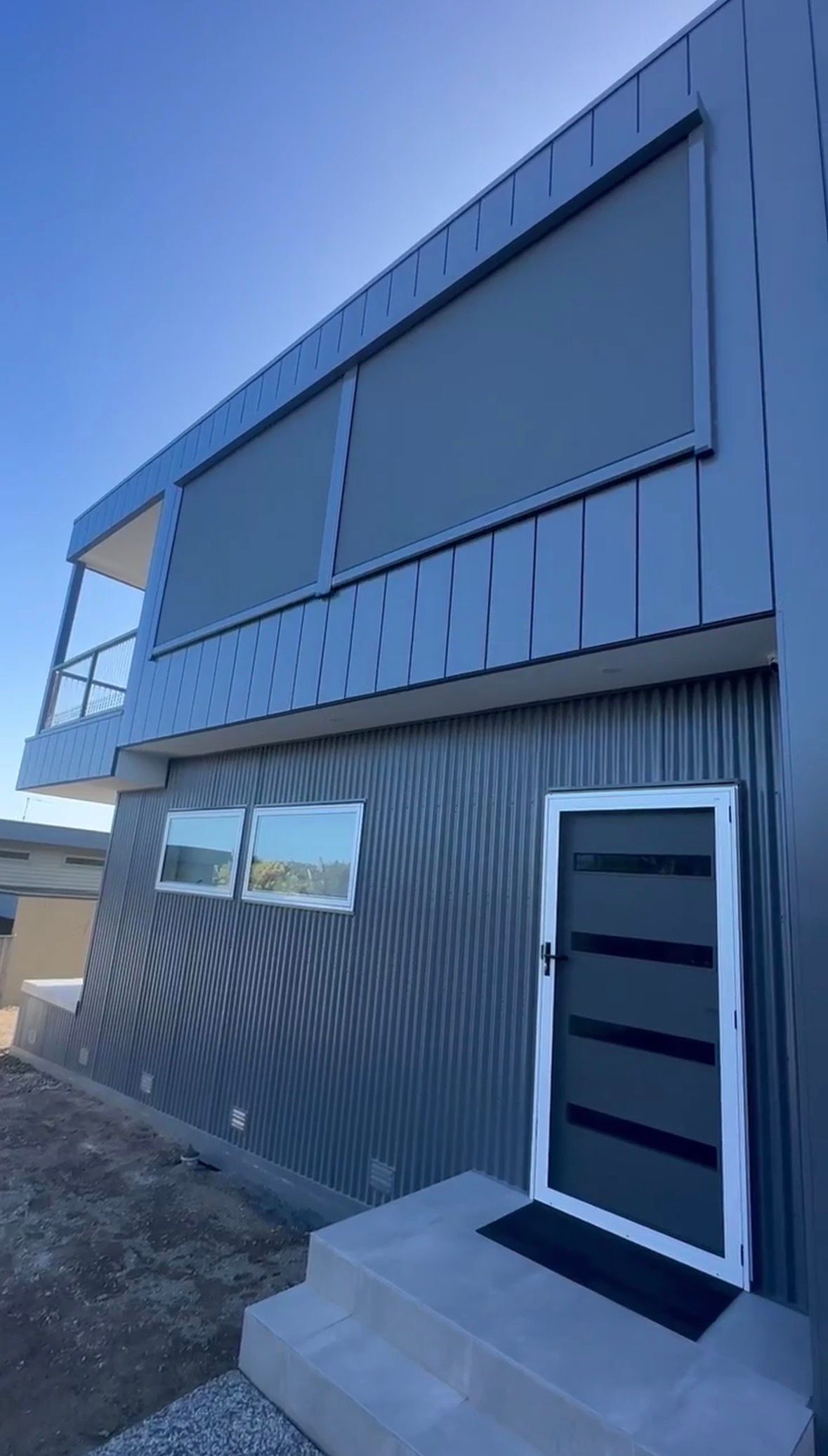 Modern two-story gray house with large windows and a black front door under construction
