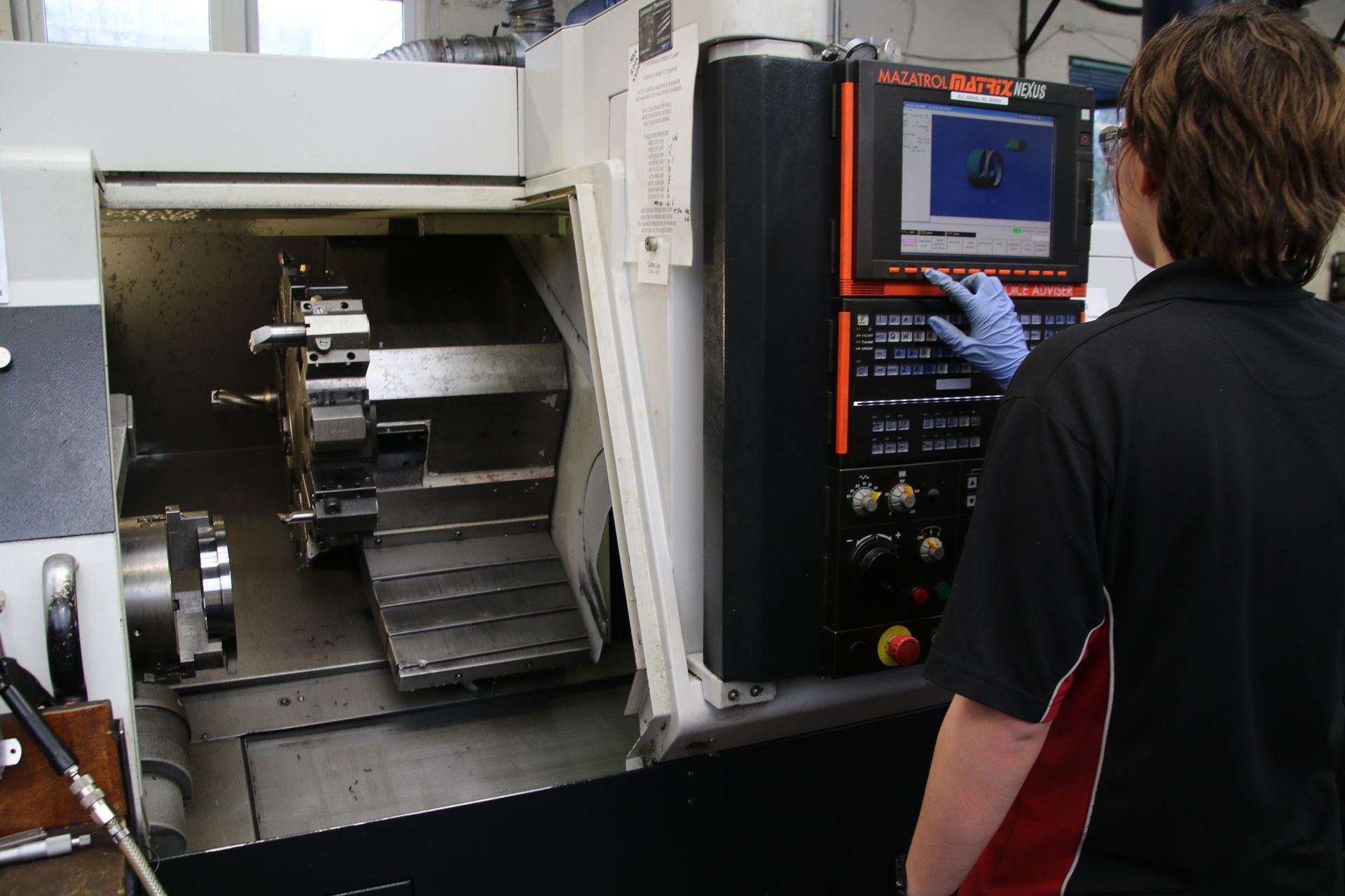 A person wearing gloves operates a CNC machine by touching the screen on its control panel.