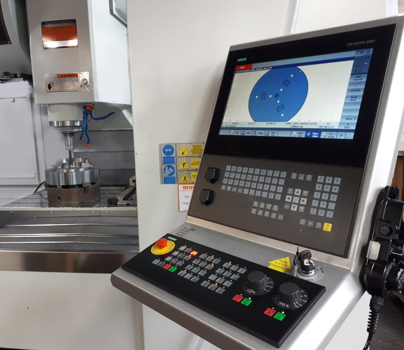A CNC milling machine control panel in the foreground with a digital interface showing a circular workpiece graphic.