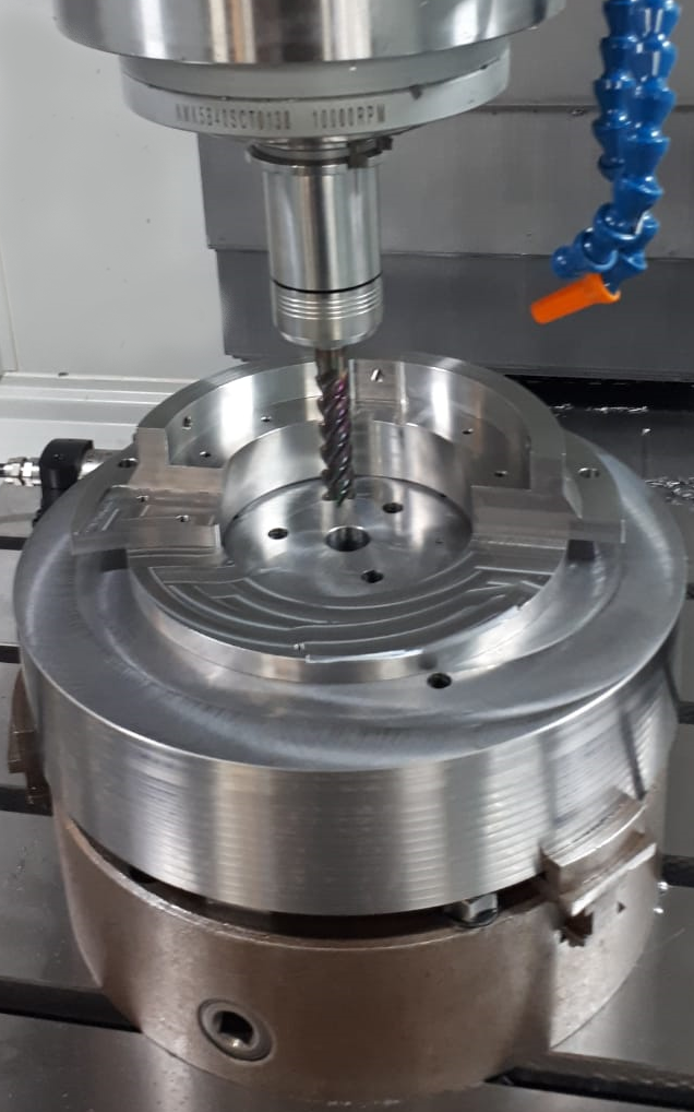 A CNC machine milling a circular metal workpiece held in a chuck.