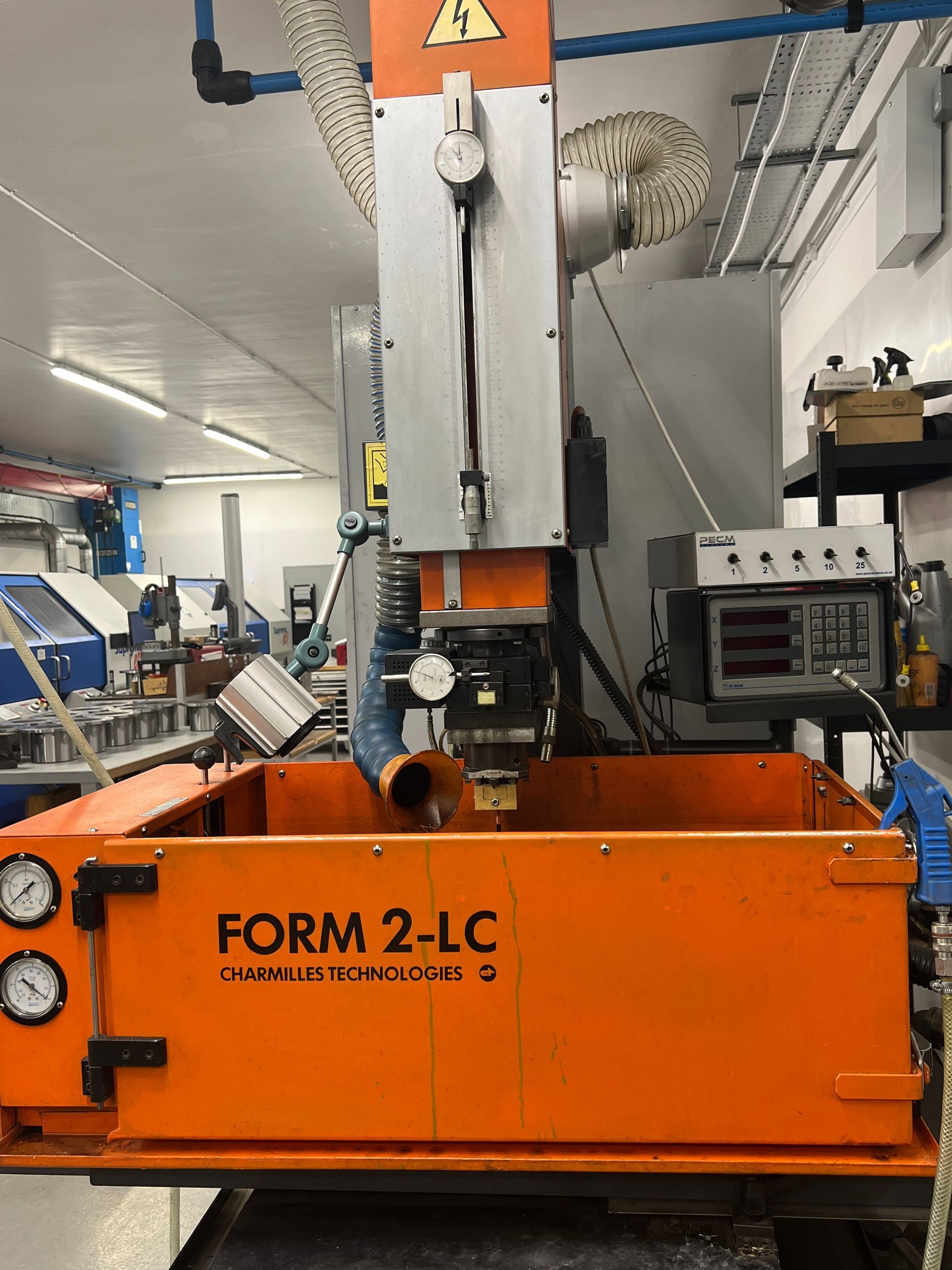 An orange FORM 2-LC industrial electrical discharge machine centered in a well-lit workshop.