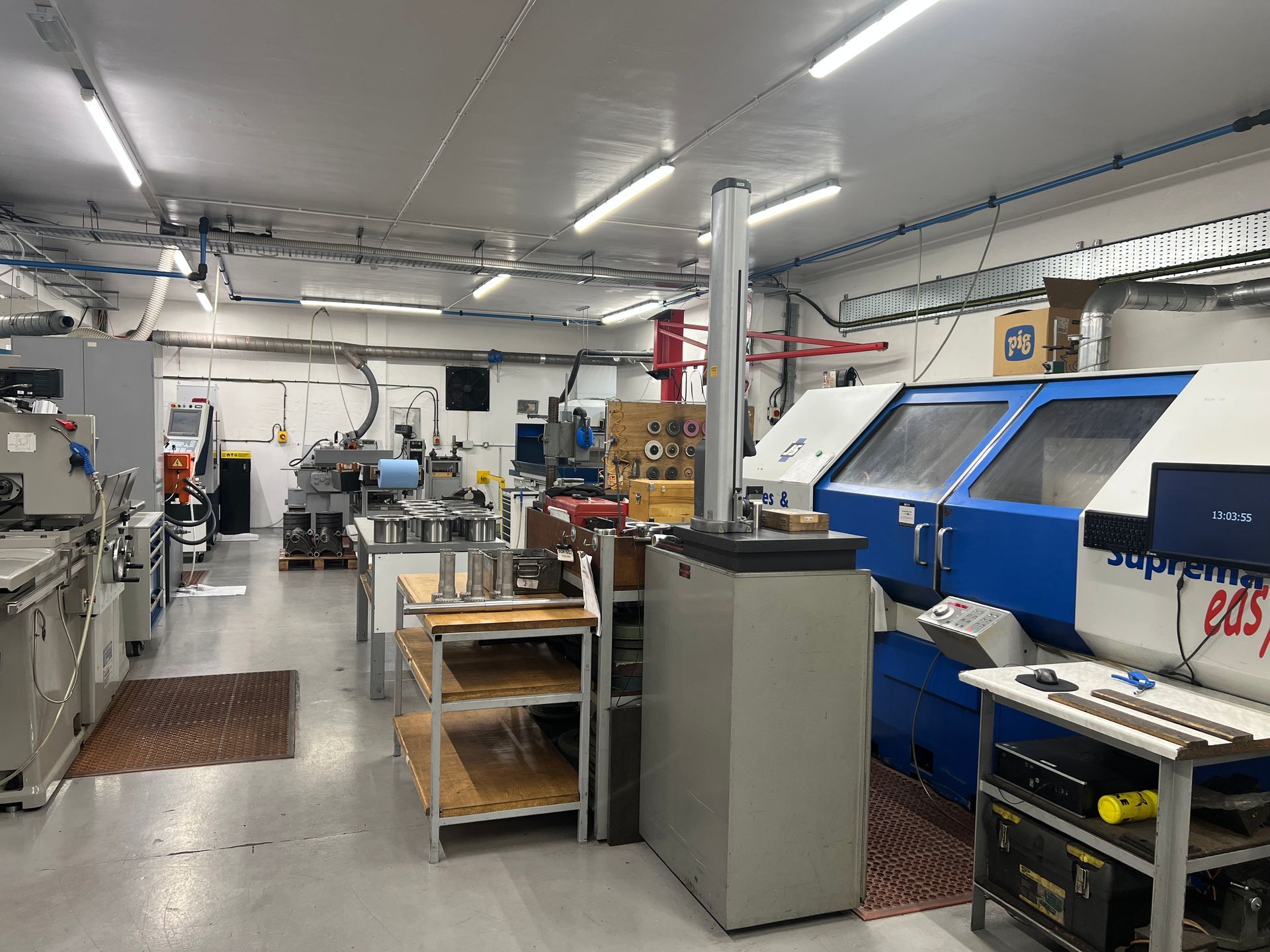 A brightly lit machine shop featuring industrial metalworking equipment, including a blue CNC lathe and metal shelving.