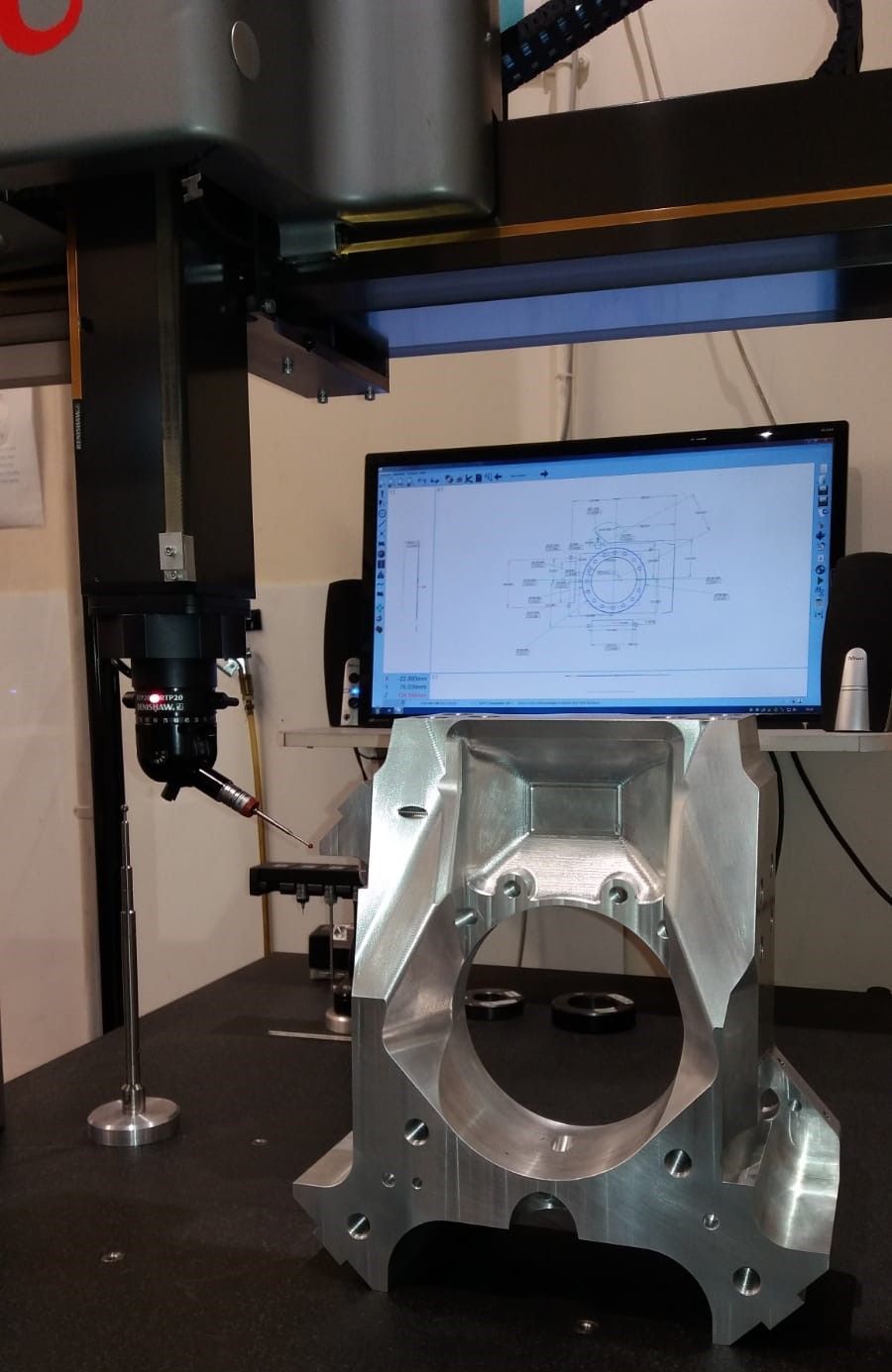 A coordinate measuring machine (CMM) inspects a machined metal industrial component on a work table.