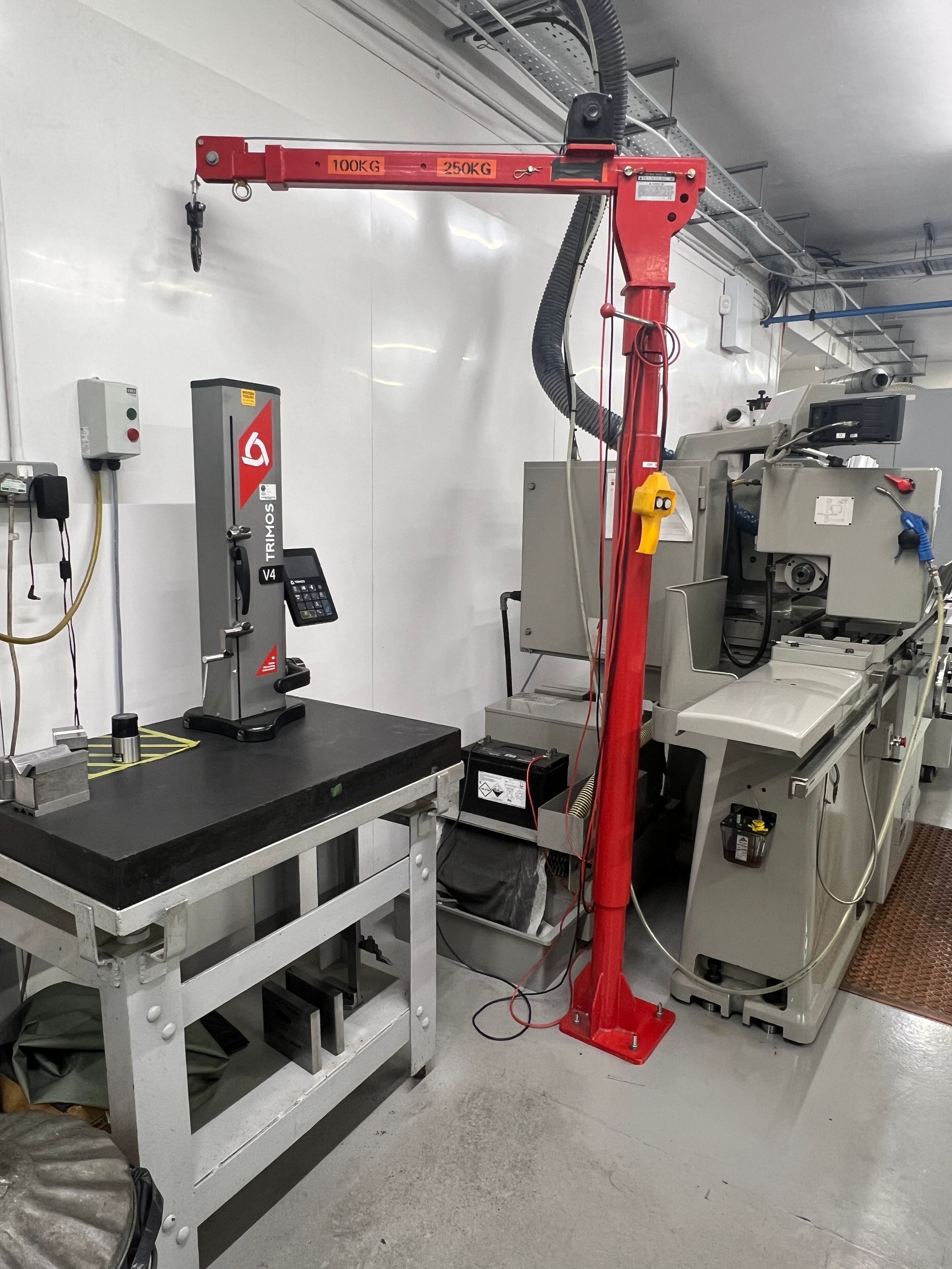A red jib crane stands in a workshop next to a metal workbench with a band saw and a large industrial machine.