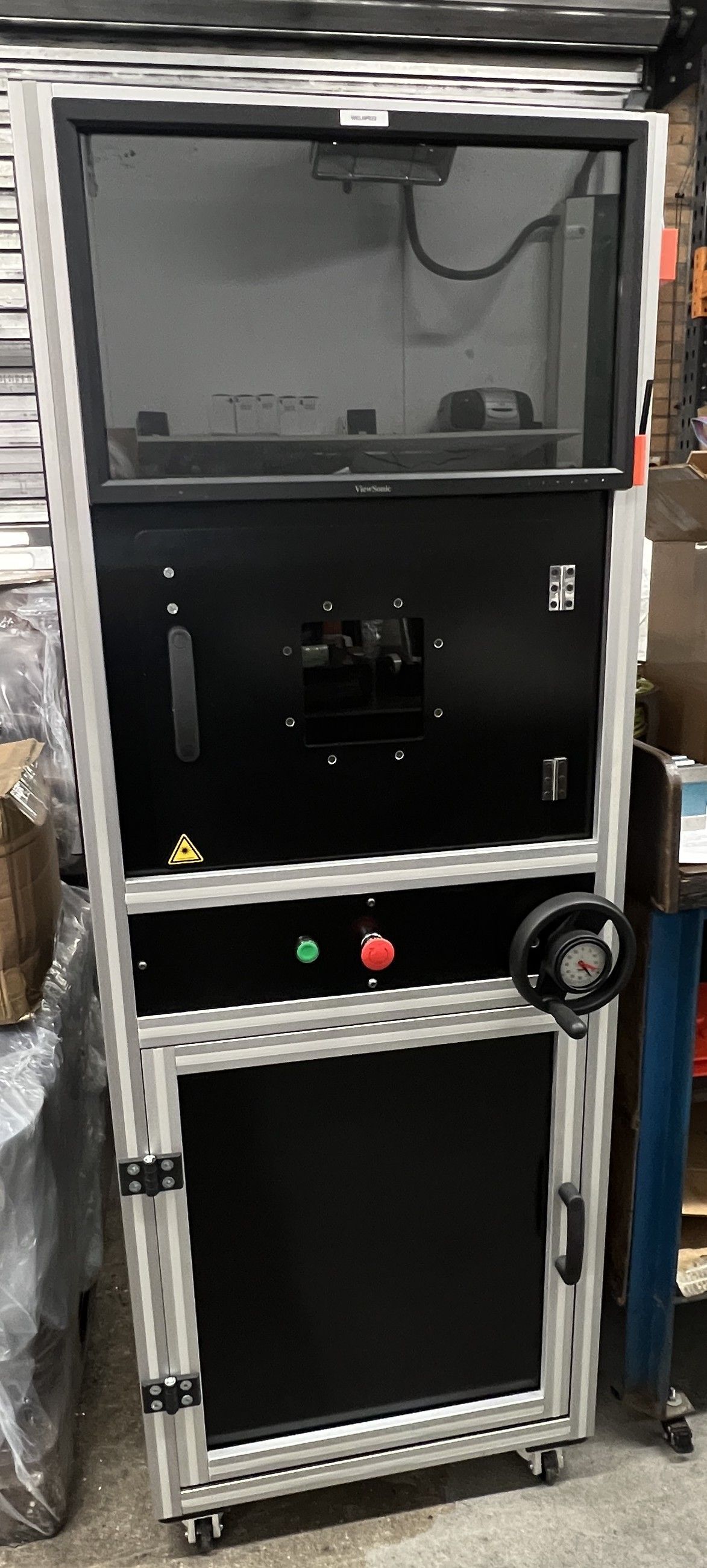 Tall black industrial cabinet with a glass top enclosure, metallic frame, and control buttons, set in a workshop.