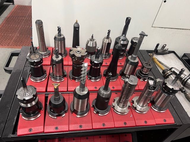 A rack filled with various metal machining tools and drill bits mounted on red plastic holders on a workshop cart.