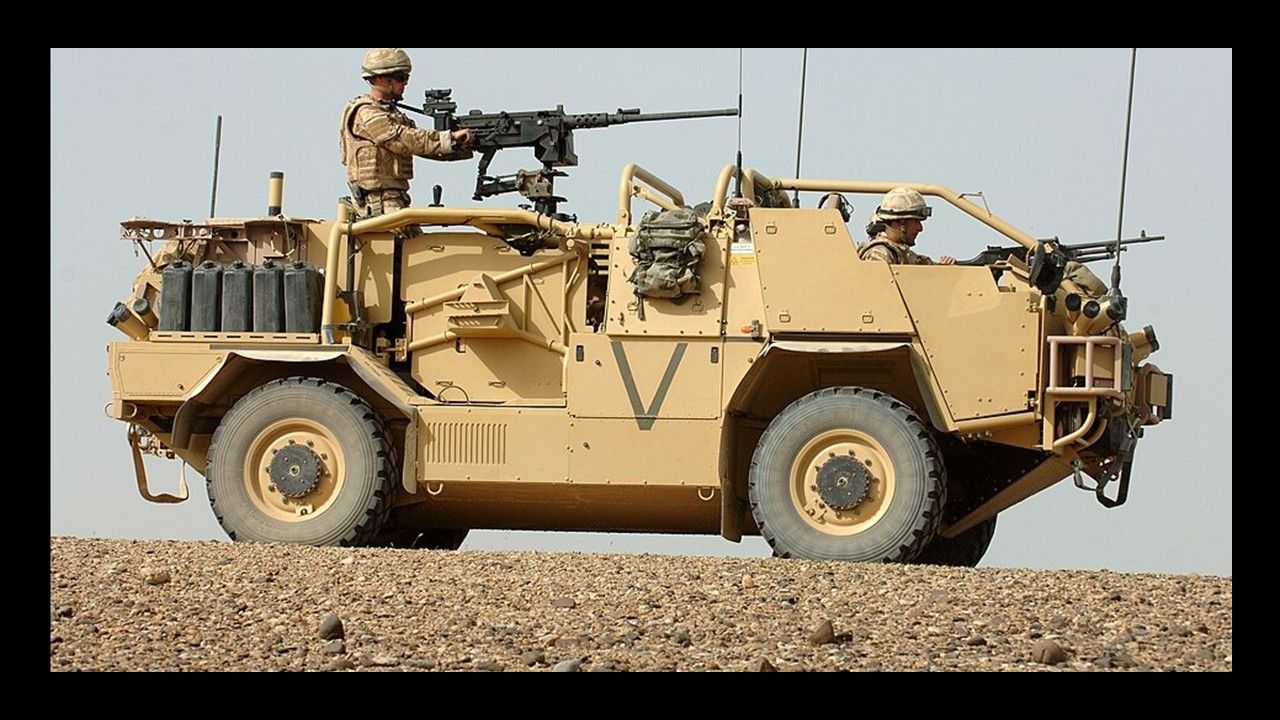 Tan military armored vehicle with a mounted gun and a soldier driving on rocky ground