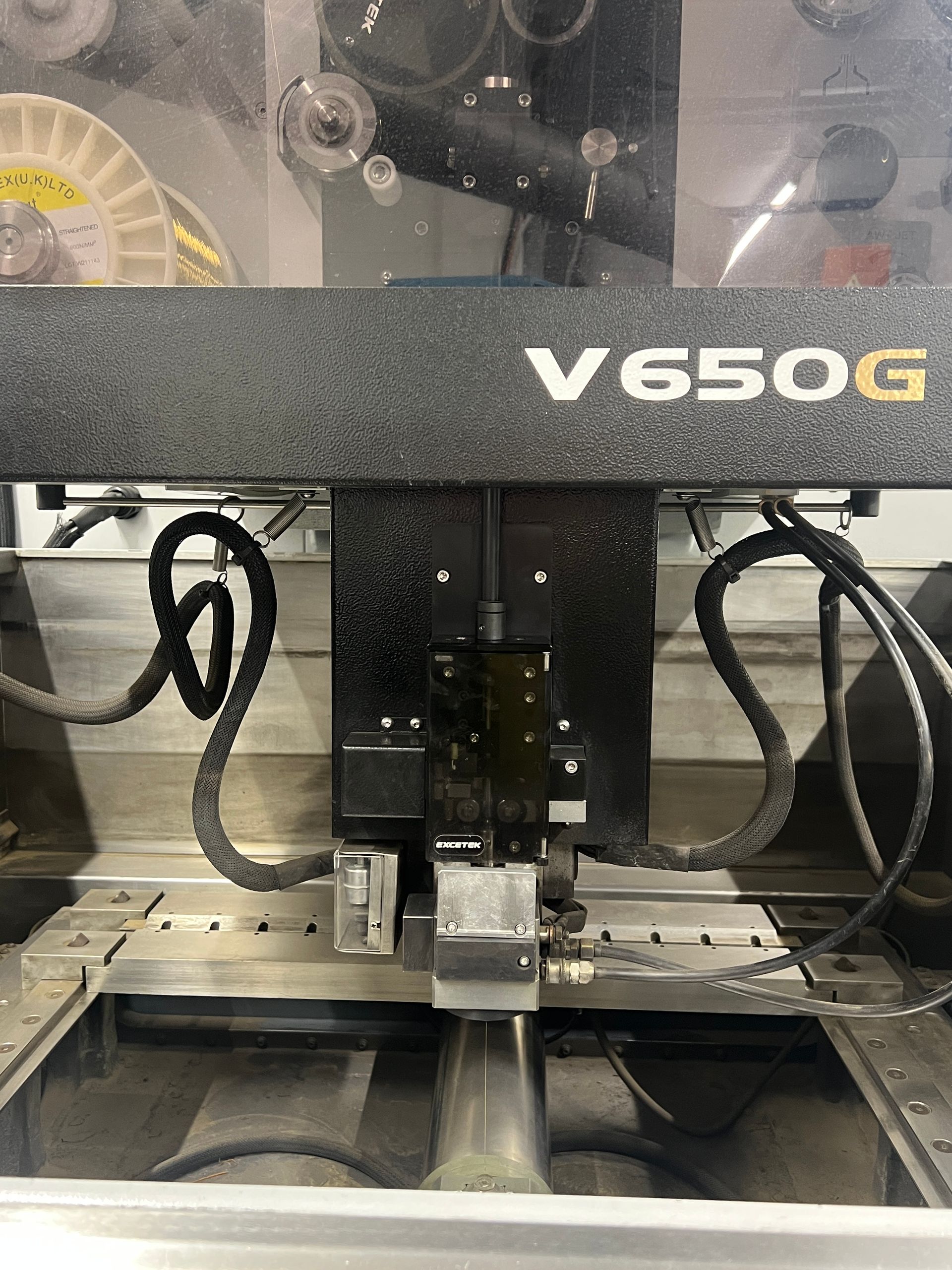 Close-up of a V650G wire EDM machine head with black housing and metallic components over a metal work bed.