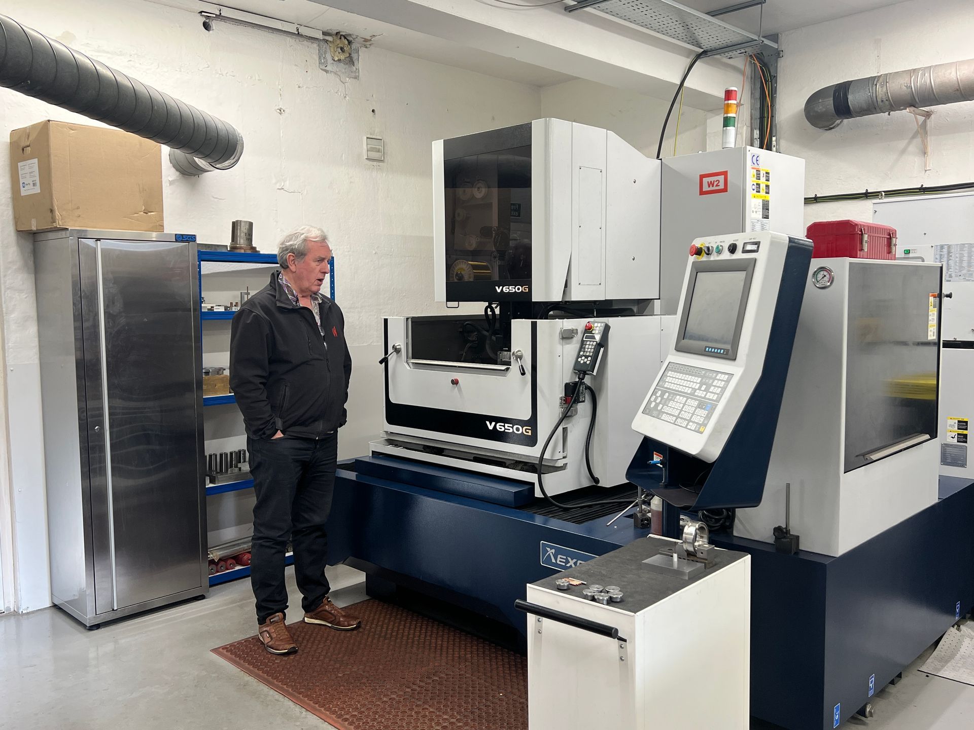 A person standing in a workshop next to a large, white and blue industrial machine with a digital control panel.