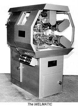 A grayscale photo of the Welmatic industrial machine, a boxy metal unit with a central component and side control panel.
