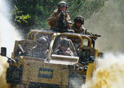 Soldiers in a tan jeep speeding through water, splashing spray in a rugged outdoor setting