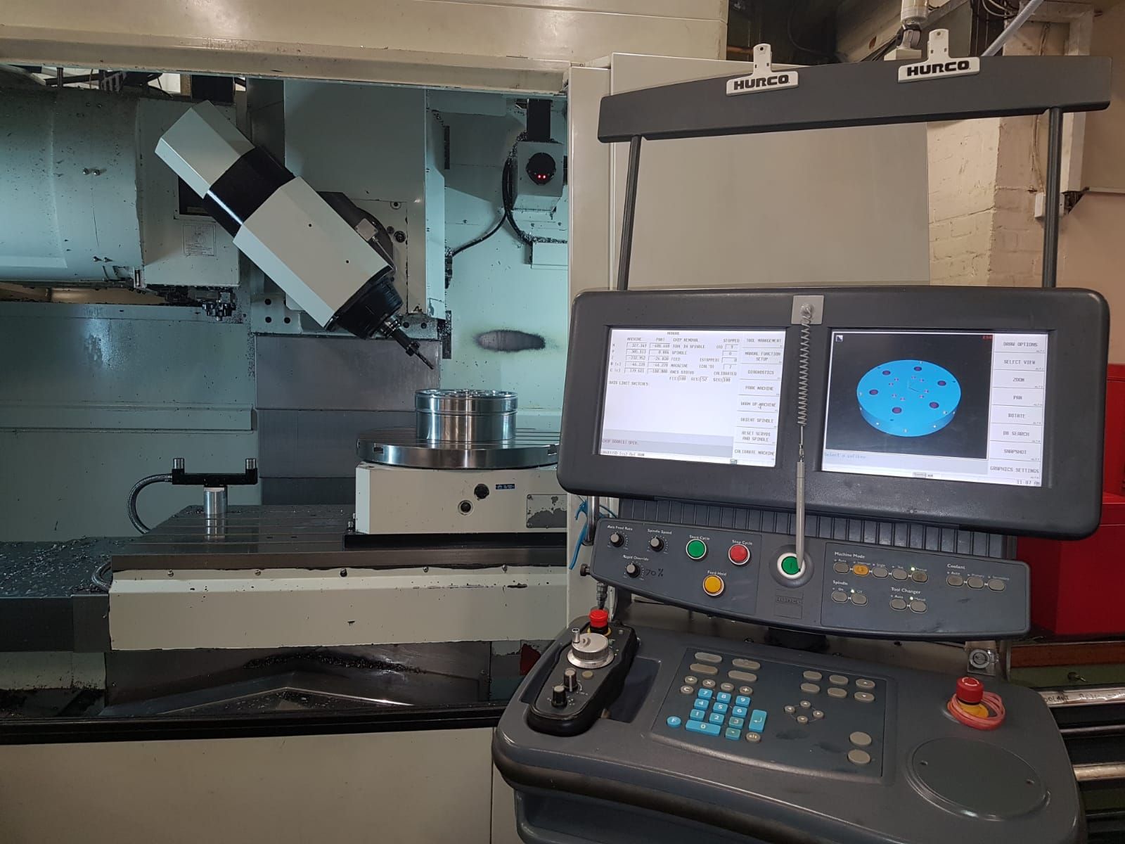 A CNC milling machine with a digital control console displaying a technical blueprint and a 3D model of a circular part.