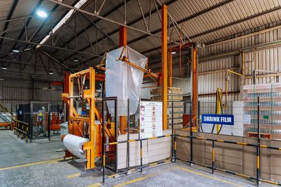 Industrial warehouse with orange machinery and fenced storage area under a metal roof