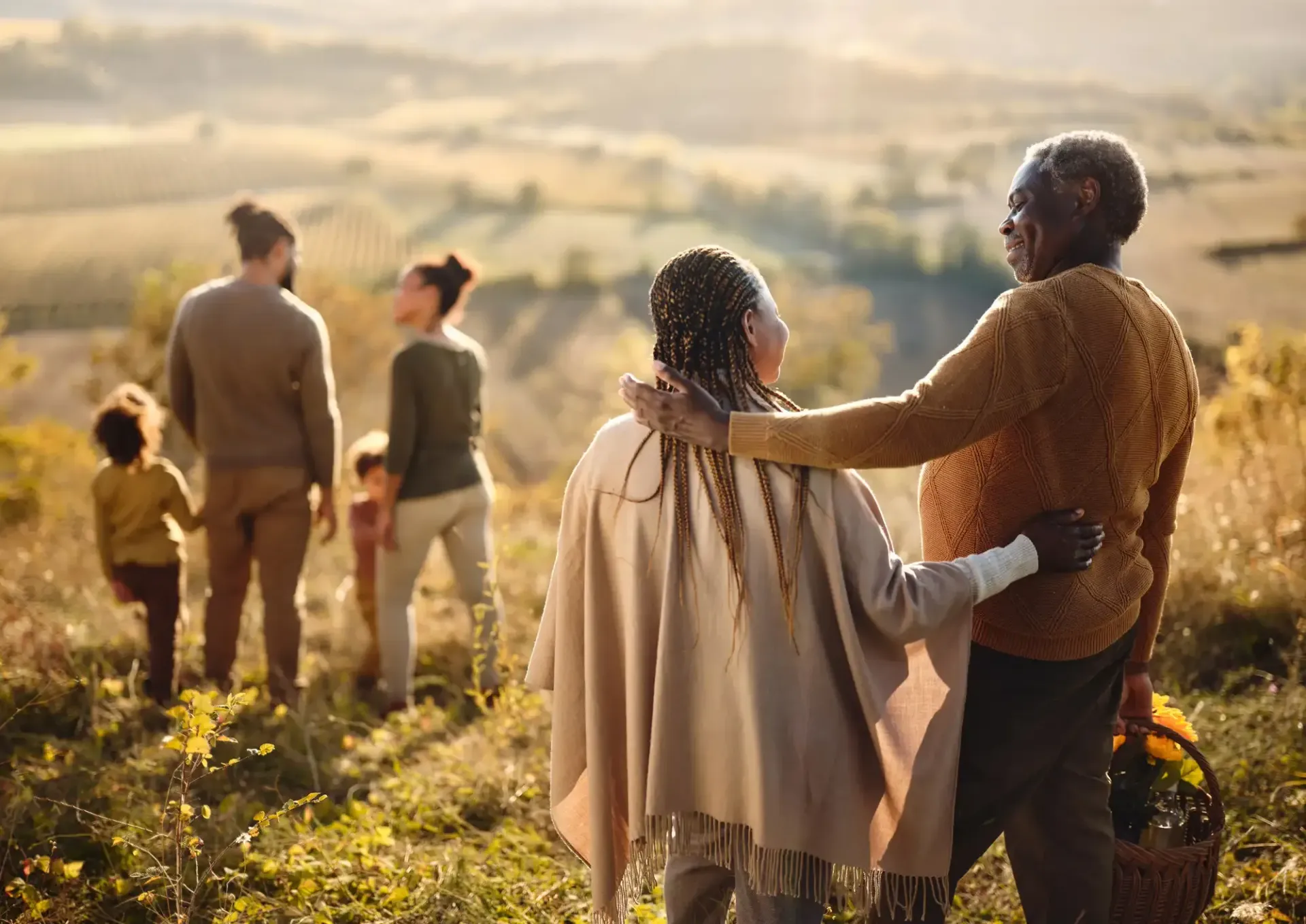 Four people stand together in a sunlit field, overlooking a hazy landscape at sunrise.