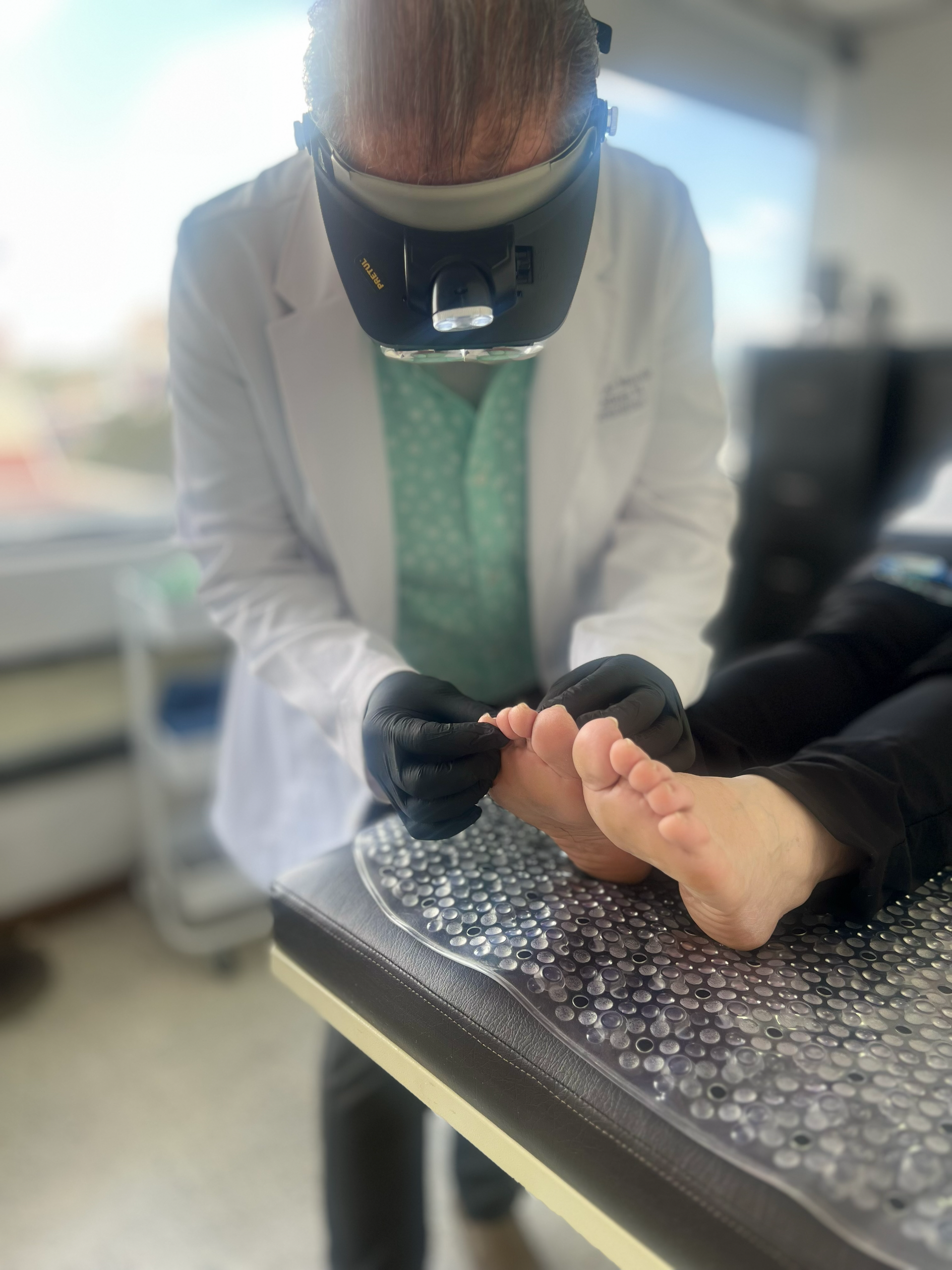 Un podólogo examina el pie de un paciente con una lupa y guantes en una clínica.