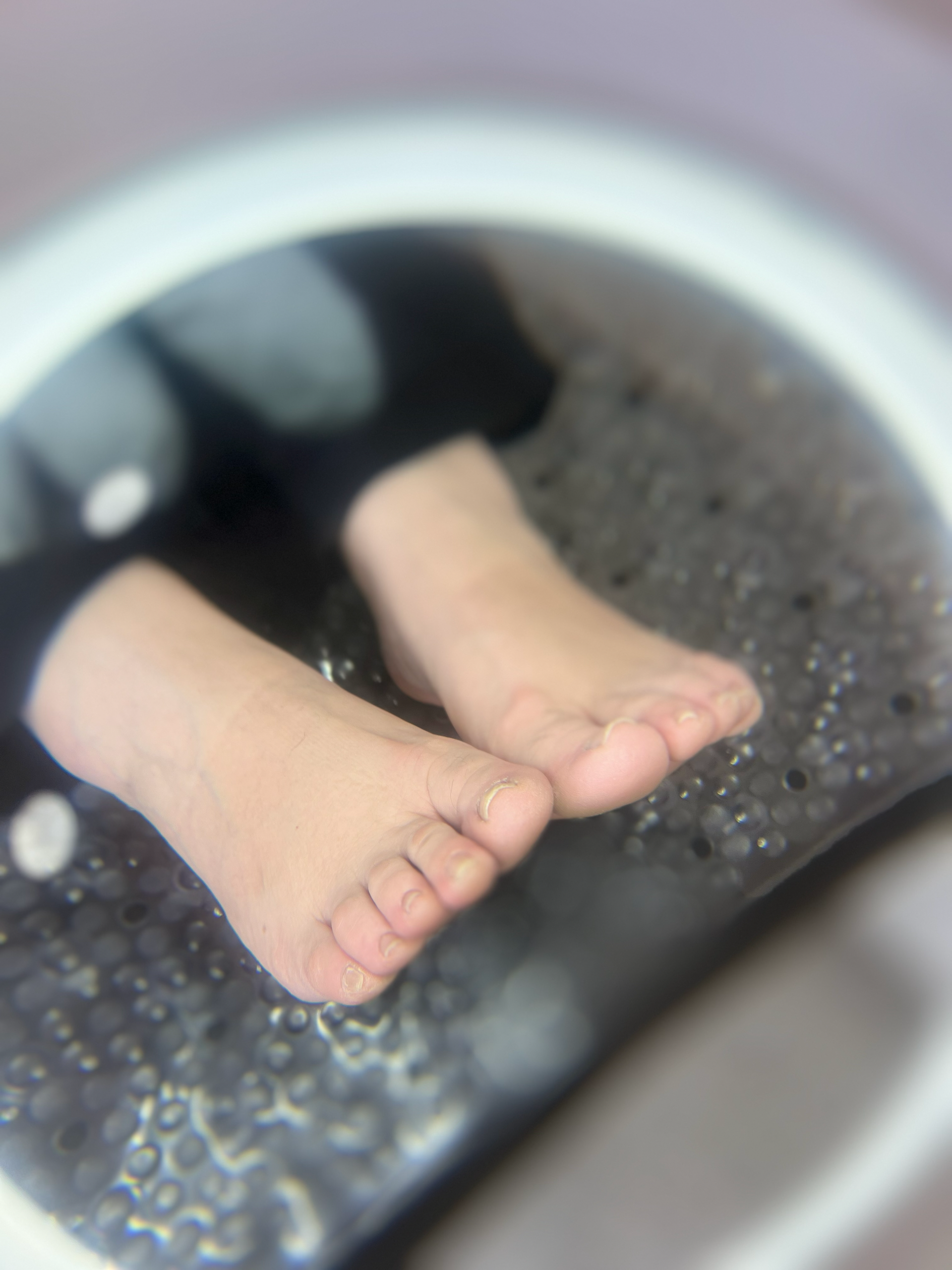 Primer plano de dos pies descalzos descansando en un recipiente oscuro lleno de agua con borde blanco.