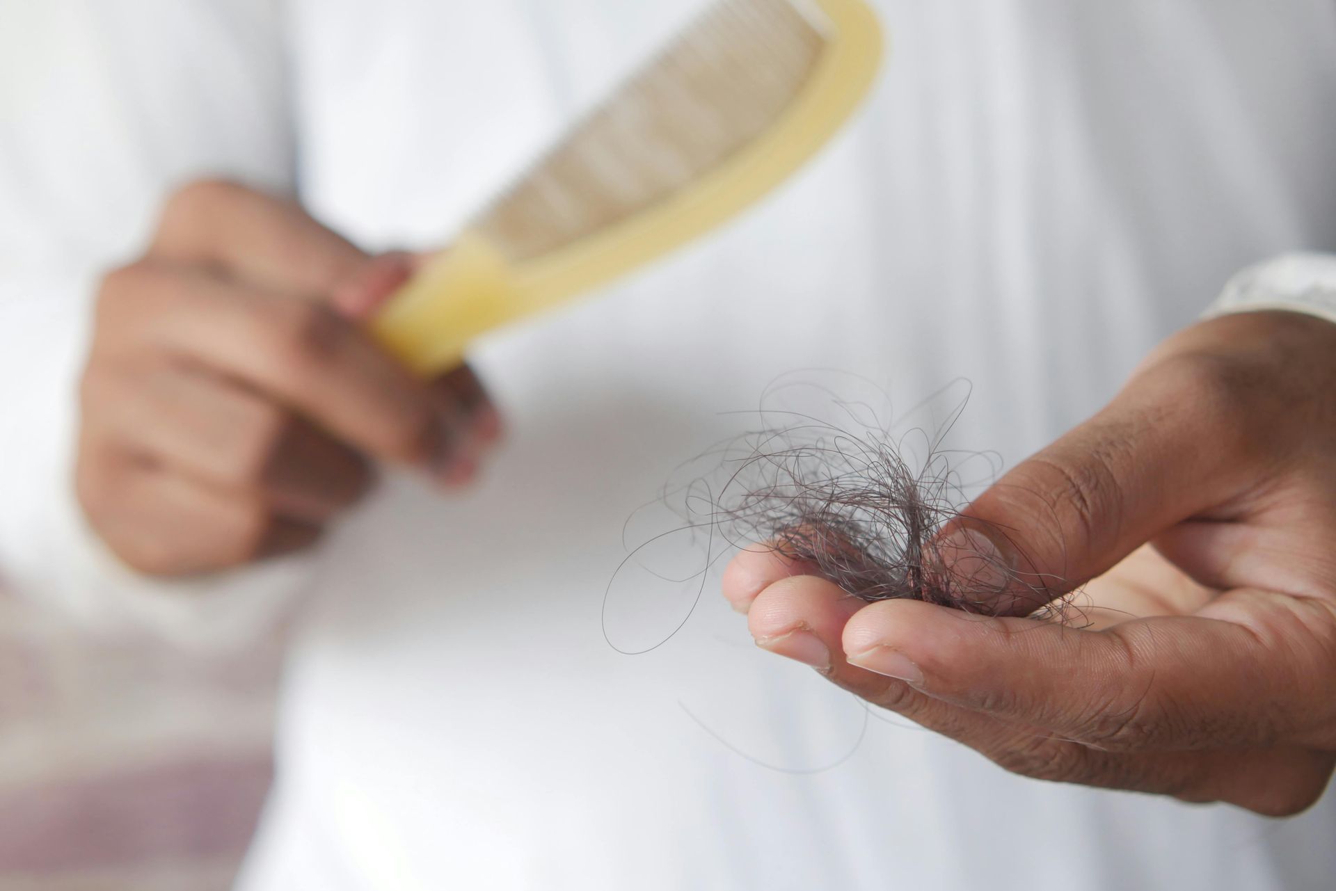 Una mano sostiene mechones de cabello mientras otra sostiene un cepillo amarillo sobre un fondo de camisa blanca.